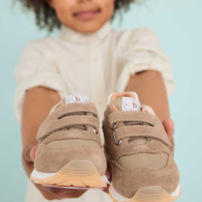 Gros plan sur un enfant tenant des baskets en daim beige à semelles blanches.