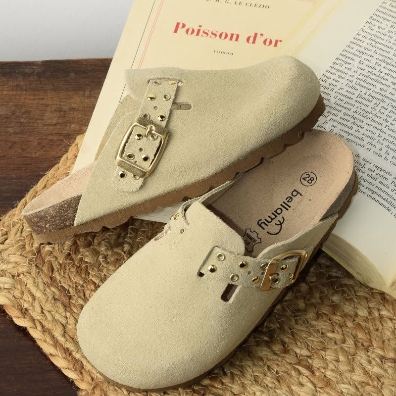 Une paire de sabots Birkenstock beiges sur un tapis tressé à côté d'un livre ouvert