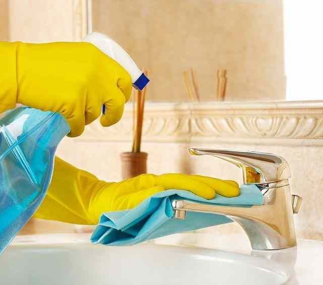 Una persona que lleva guantes amarillos está limpiando un grifo del fregadero con un paño.