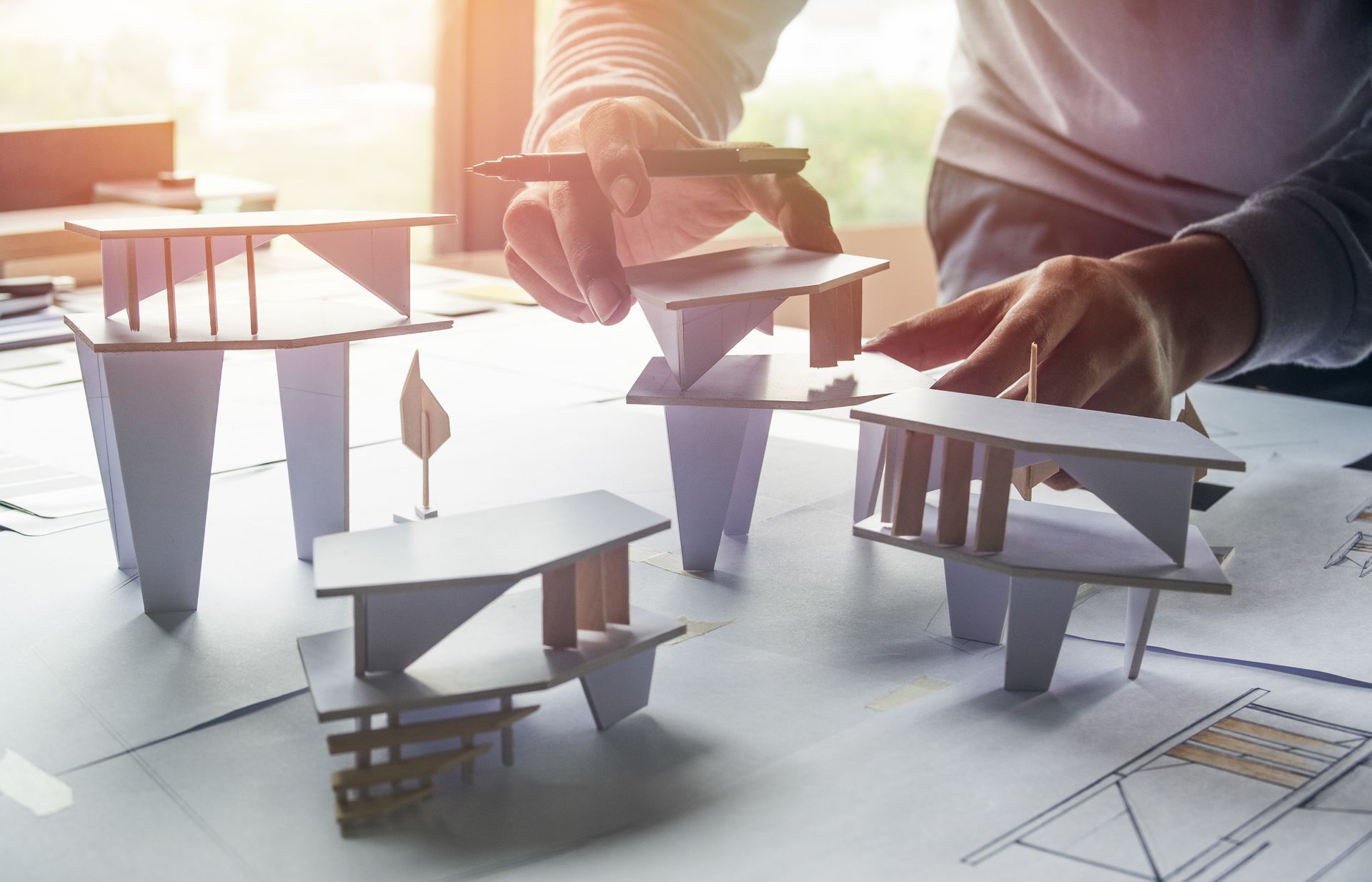 Arquitecto revisando diseños de modelos de edificios sobre una mesa, sosteniendo un bolígrafo.