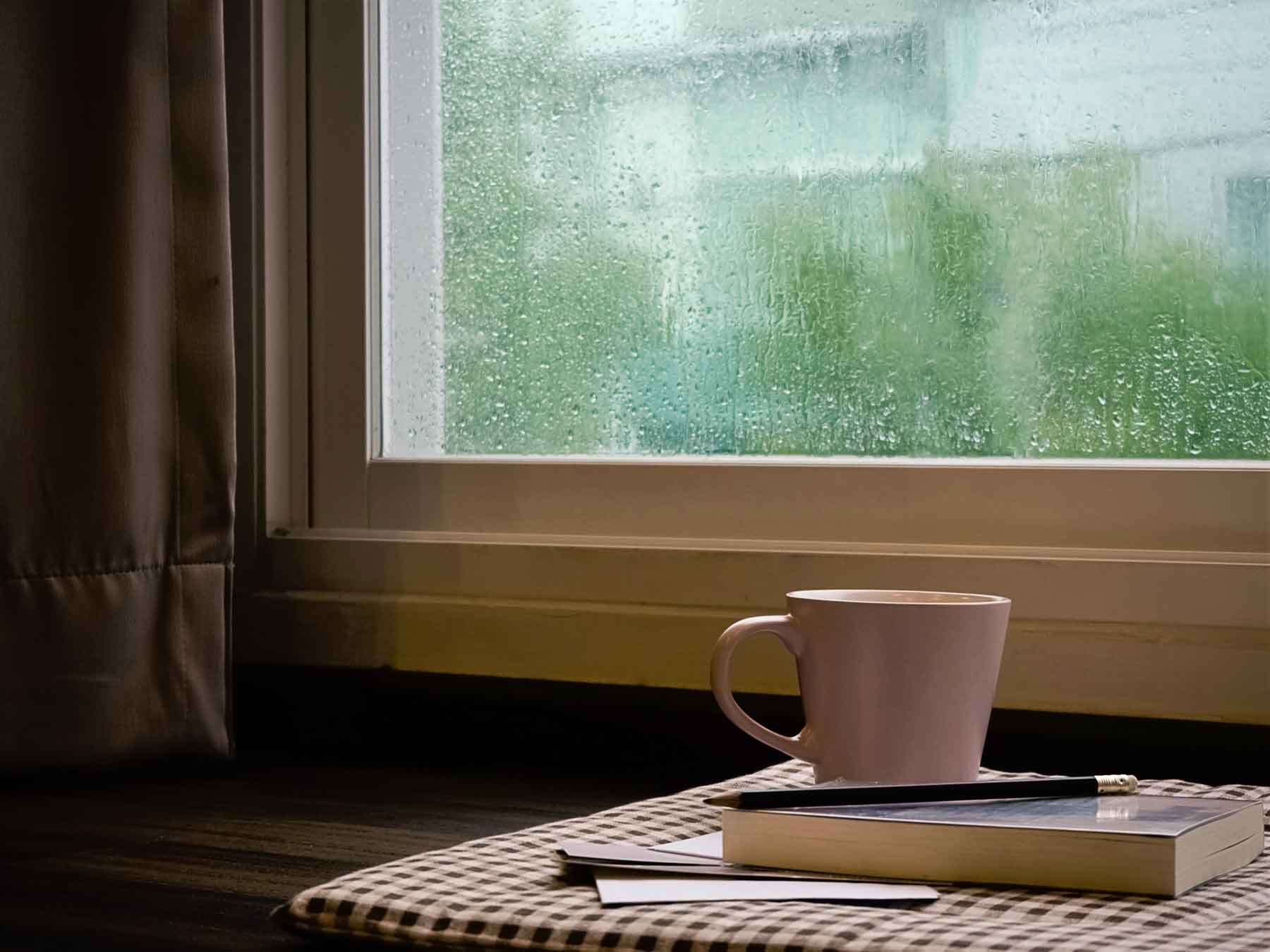 Pluie coulant sur une fenêtre et tasse de café avec un livre et un crayon