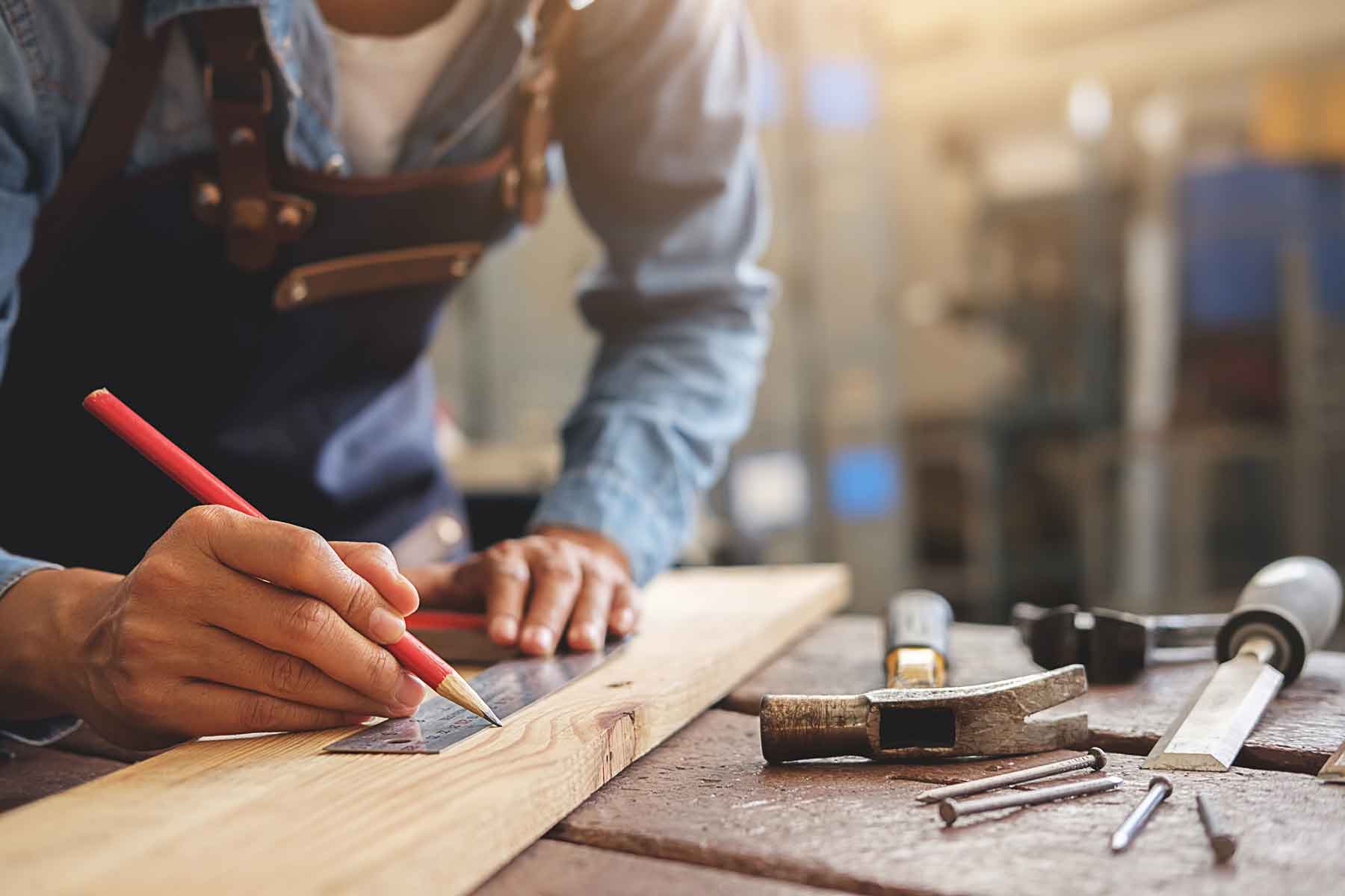 Menuisier traçant une mesure sur une planche avec un crayon de papier et une règle de mesure