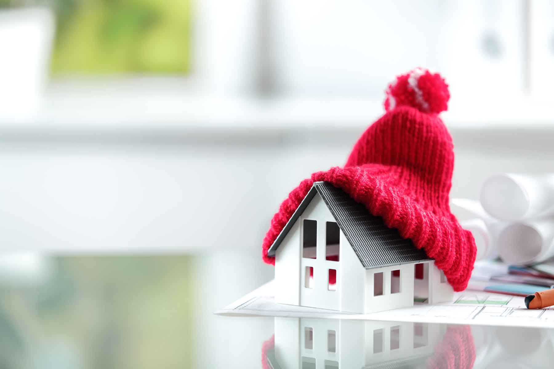 Maquette de maison sur un plan d'architecte avec un bonnet rouge au niveau de la toiture