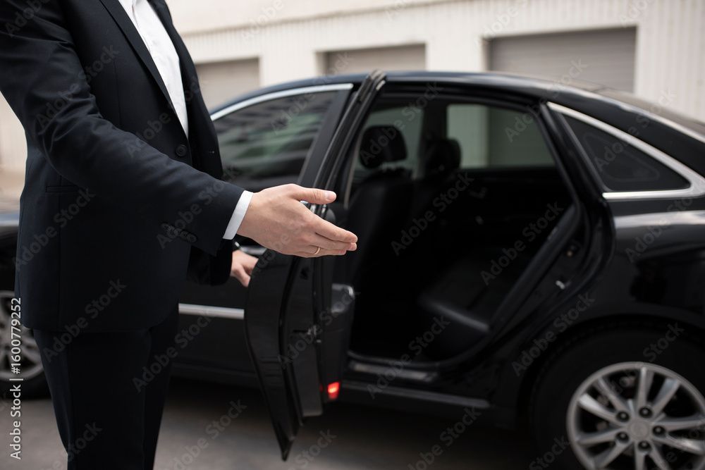 Person im Anzug öffnet die Tür eines schwarzen Autos und bietet Hilfe an.