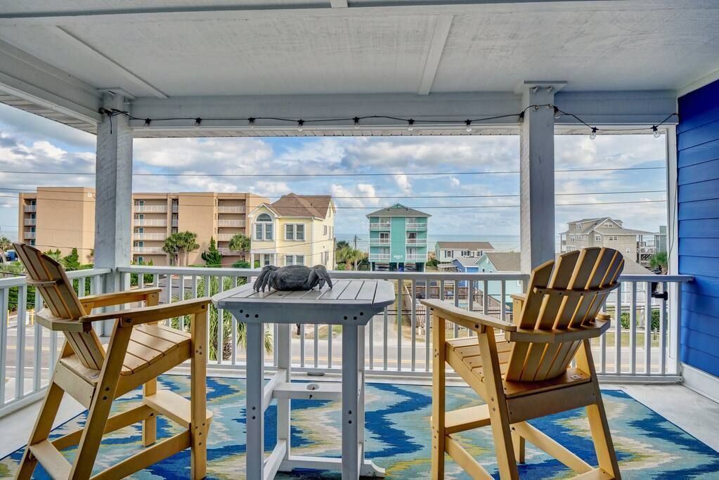 Two wooden chairs face a small table on a porch with an ocean view.