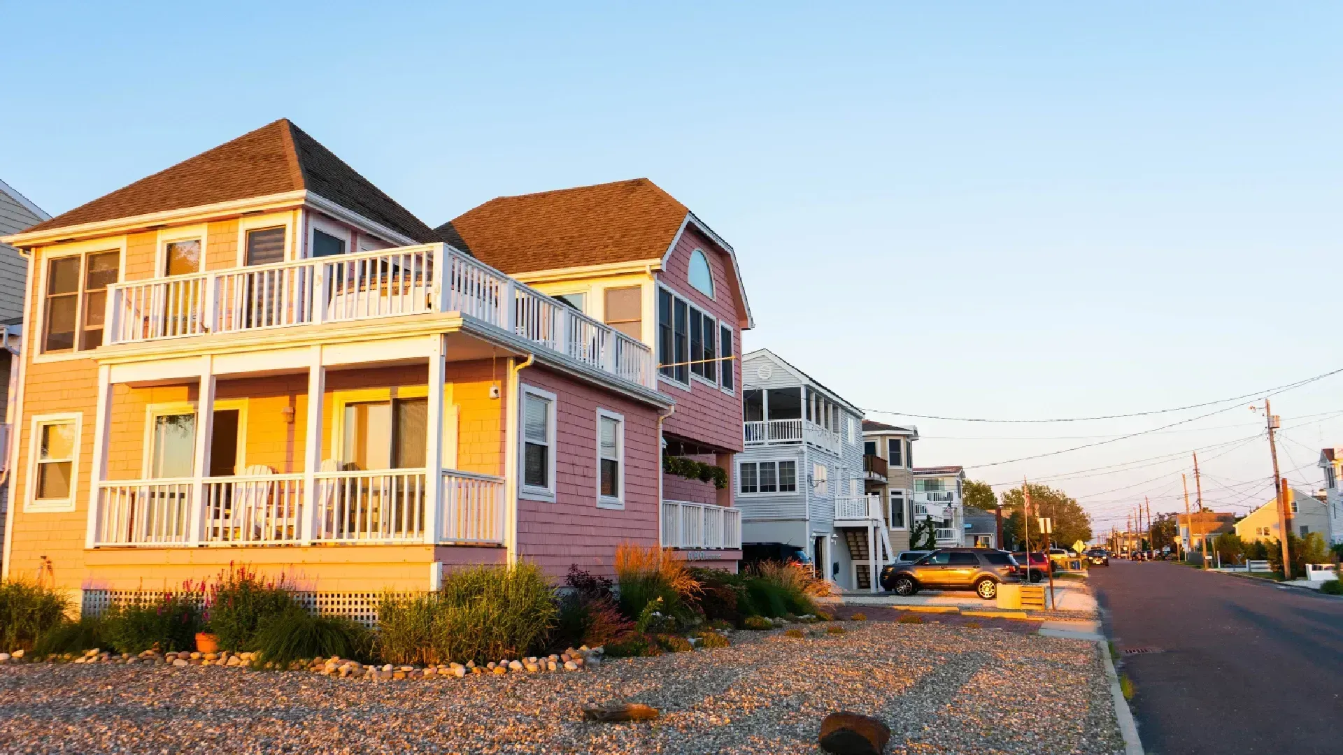 Colorful houses with balconies line a street near the beach at sunset.