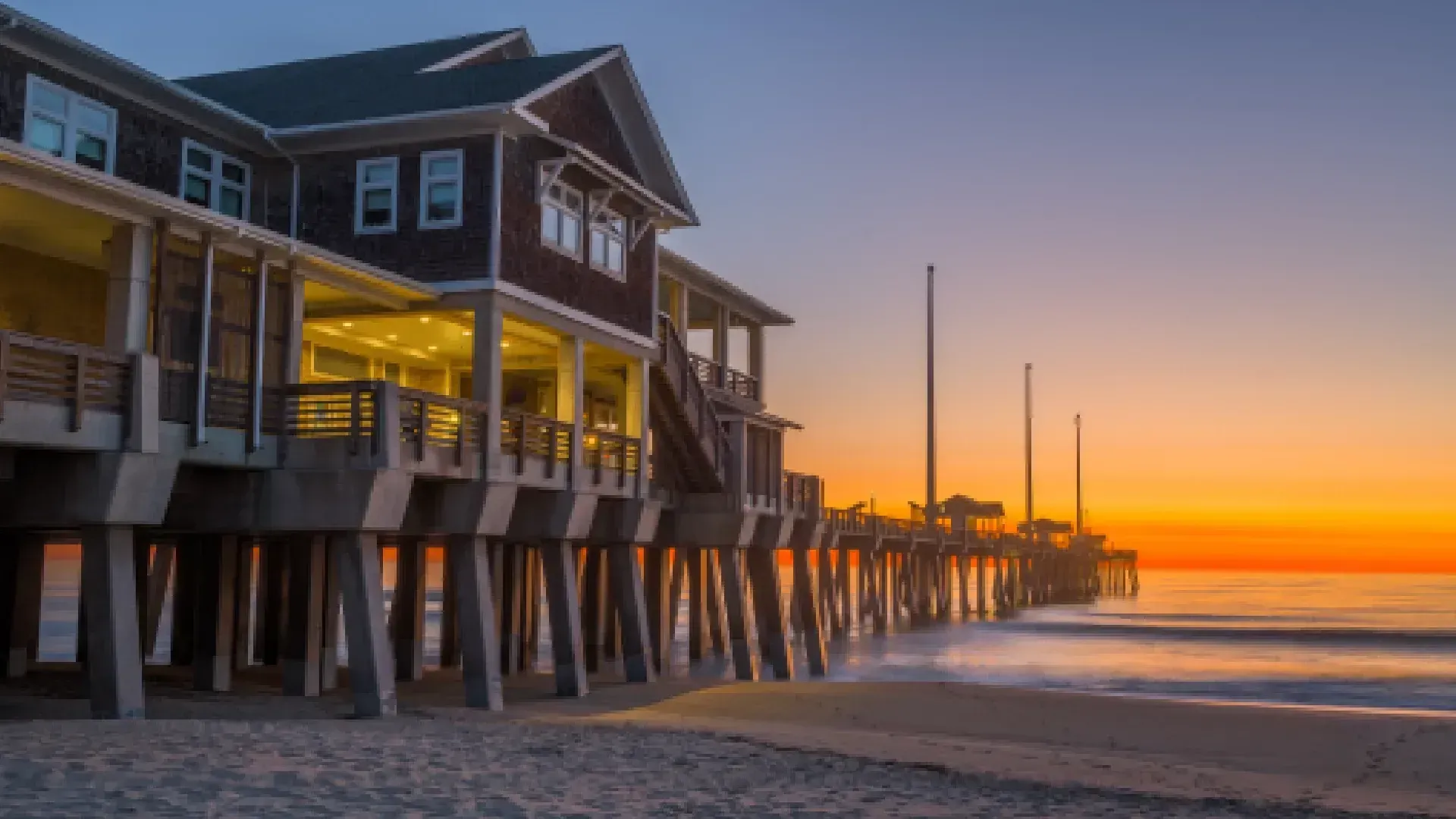Wooden pier and building at sunset with orange and blue sky.