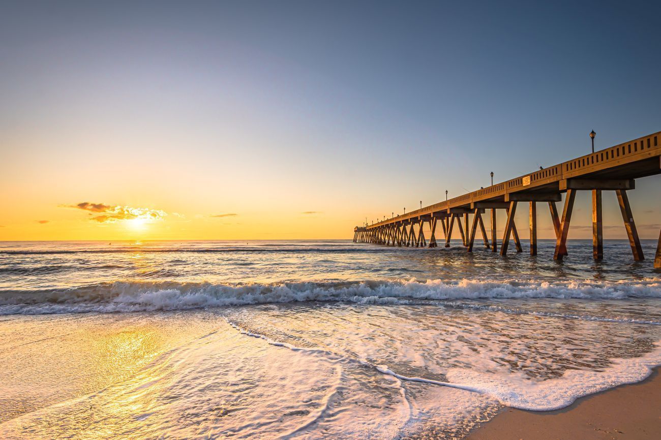 Ocean pier at sunset with golden light reflecting on the water.