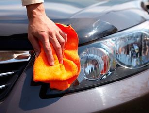 Una persona está limpiando el faro de un coche con una toalla naranja.