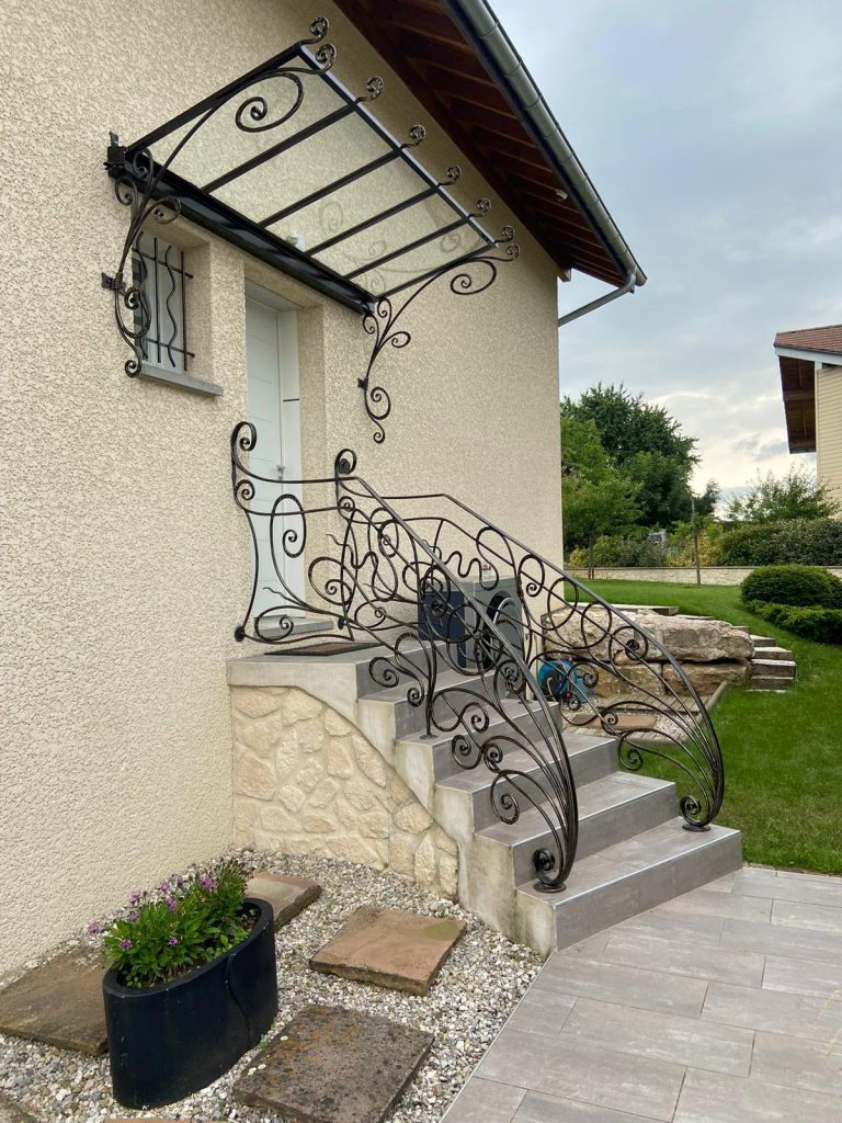 Rambarde et marquise en fer forgé noir au-dessus d'une porte d'entrée avec marches