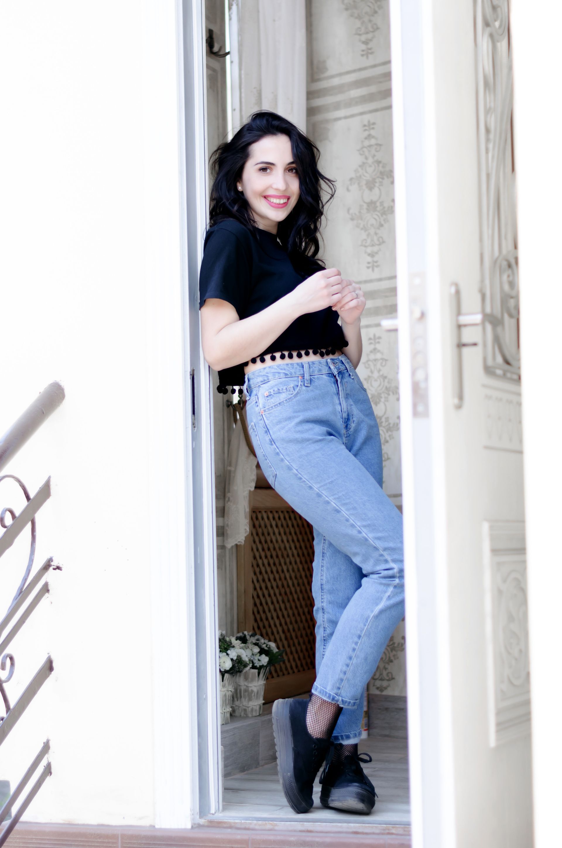 Femme en haut noir et jean appuyée dans l'embrasure de la porte