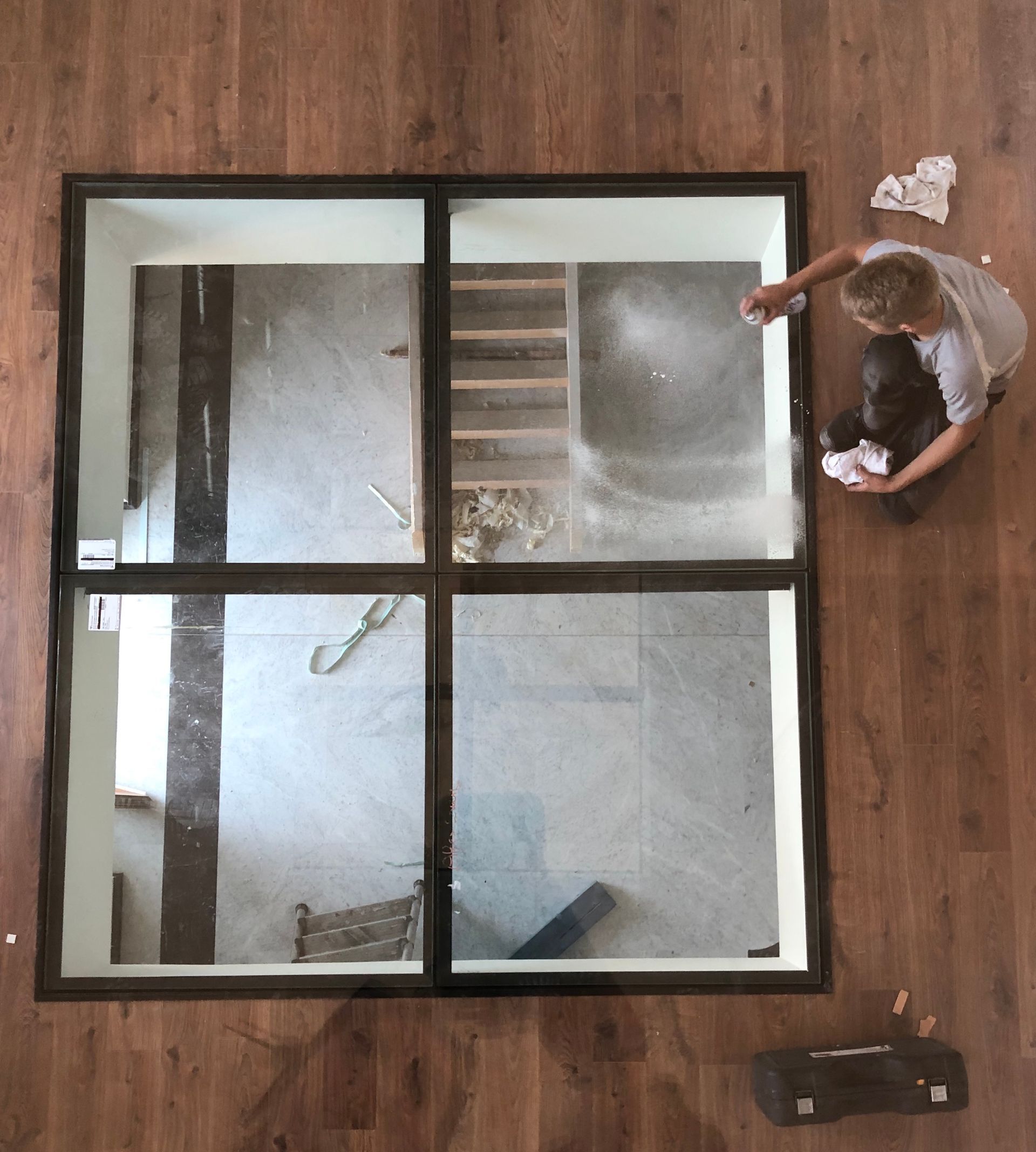 Une personne nettoie une verrière encastrée dans un parquet, révélant une pièce en dessous