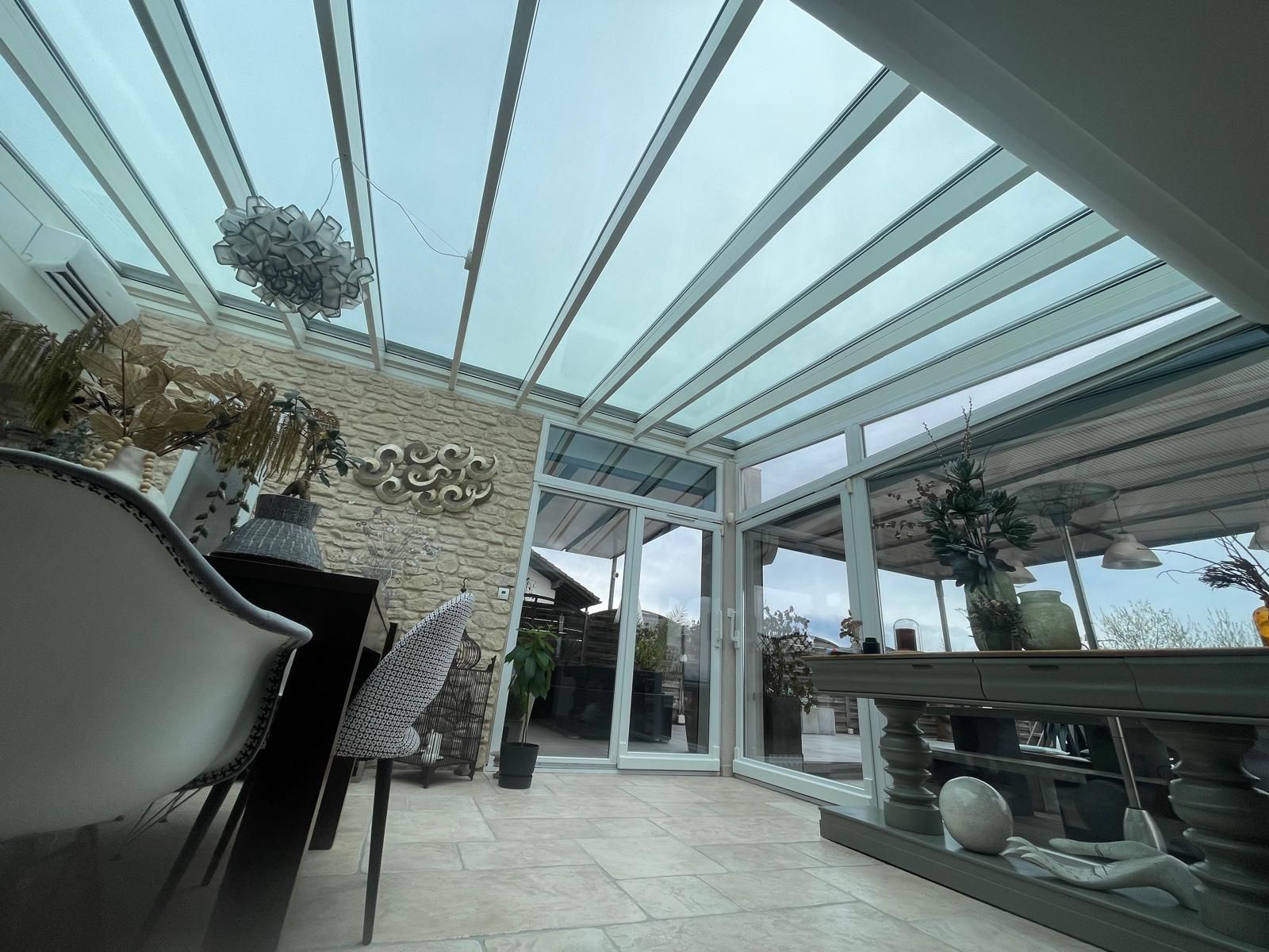 Intérieur d'une véranda avec toit en verre et mur en pierre, une table et des chaises