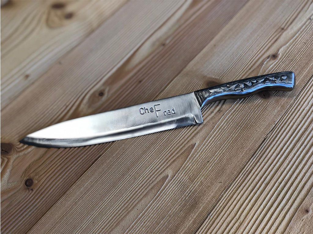 Couteau de chef posé sur une surface en bois, gravure « Che-F-red » sur la lame.
