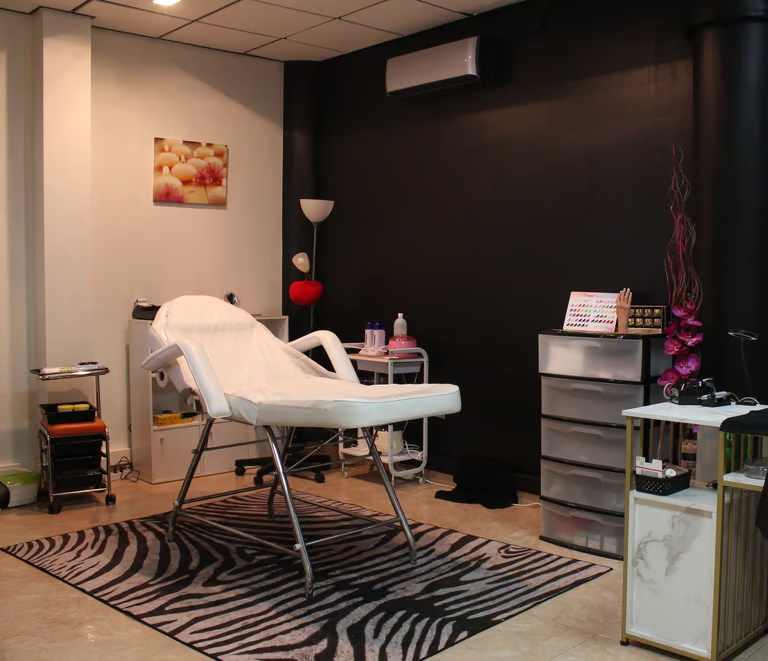 Sala de masajes con sillón de tratamiento blanco, alfombra de cebra, armarios y luz tenue.