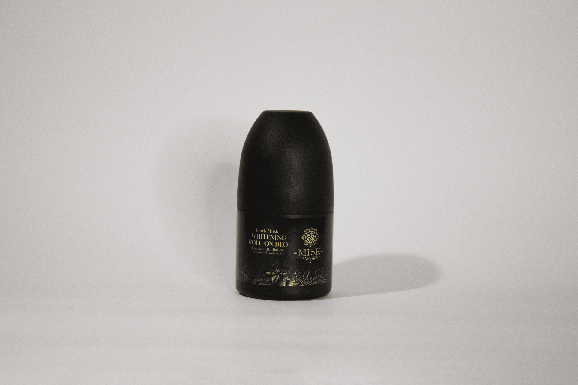Botella cilíndrica negra centrada sobre una superficie blanca con una tenue sombra y texto de etiqueta dorado.