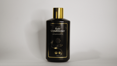 Botella de acondicionador para el cabello negra y dorada con tapa dorada sobre un fondo claro liso.