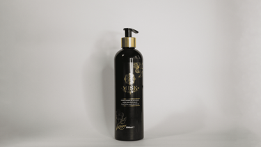 Botella de champú o loción con dosificador, de color negro y dorado, sobre un fondo blanco liso.