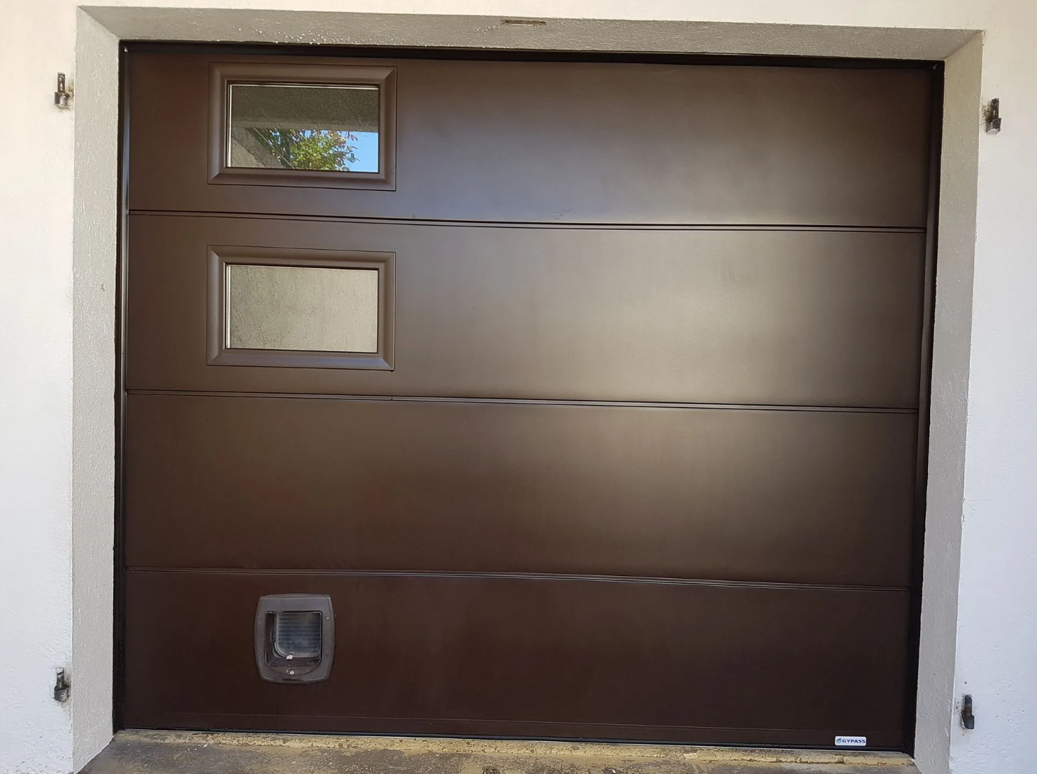 Une porte de garage marron avec deux vitrages et une chatière