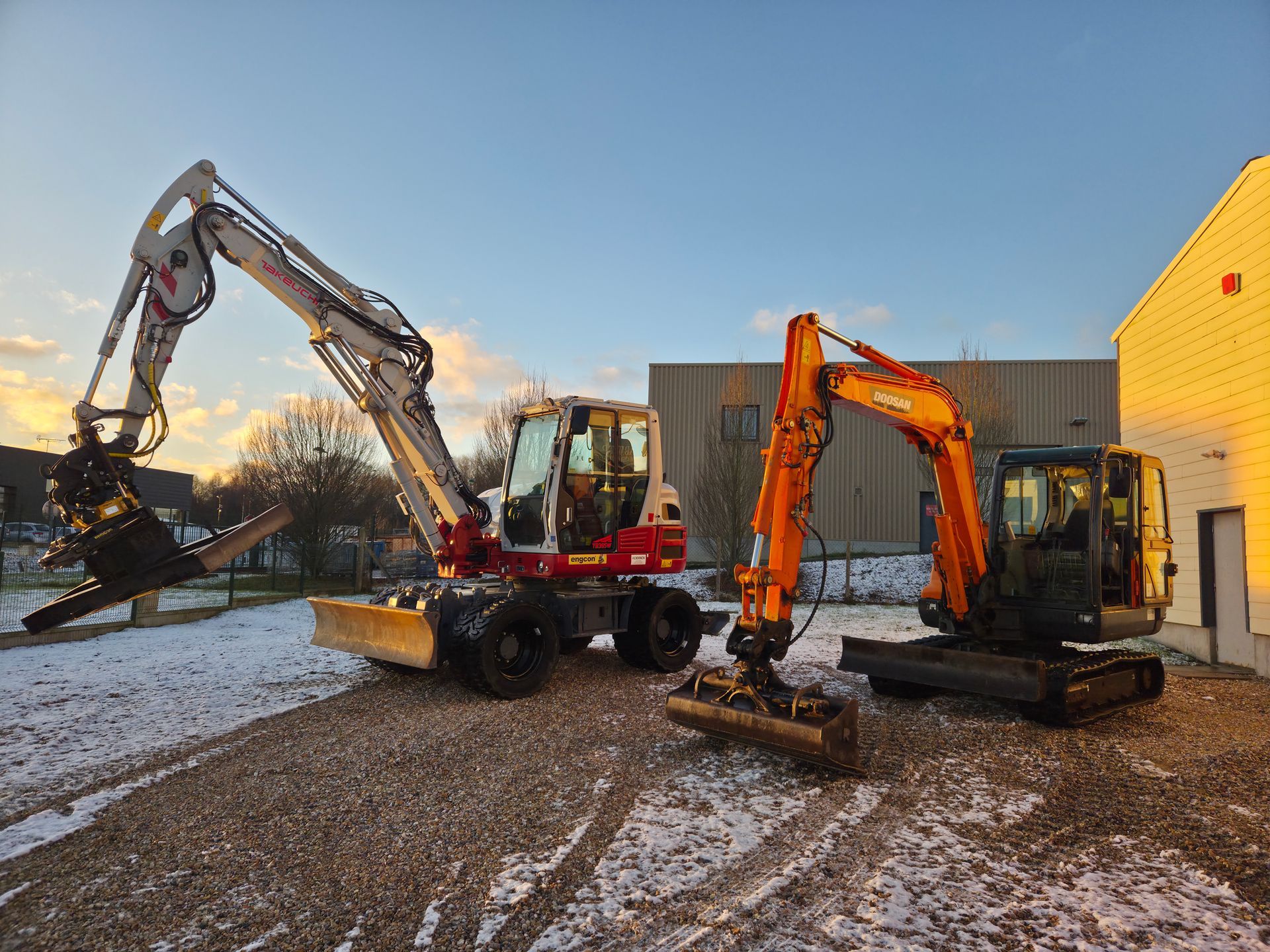Deux excavatrices creusent sur un chantier enneigé au coucher du soleil