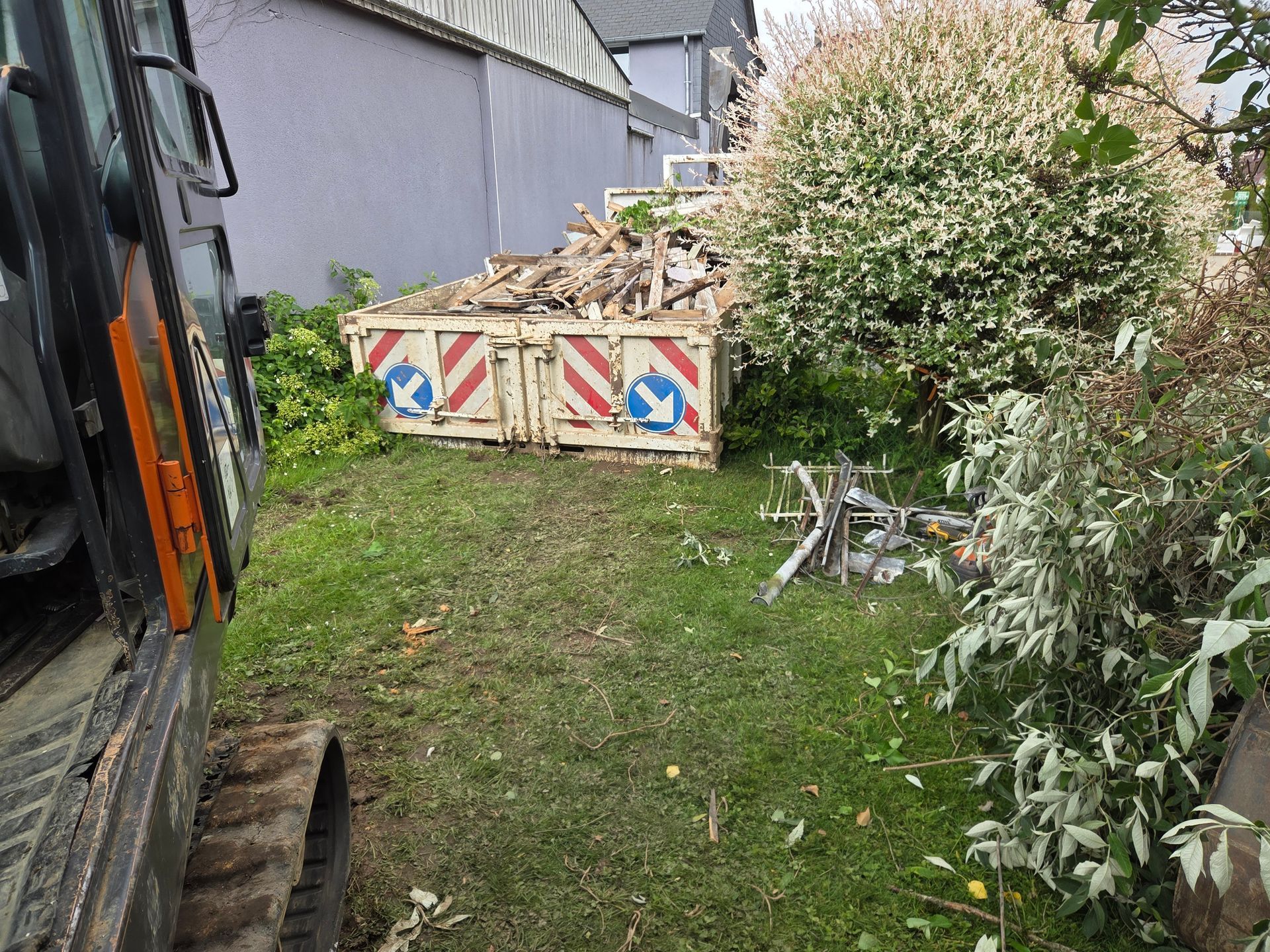 Remorque à côté d'une cour herbeuse avec barrière rayée, caisses et buissons le long d'un bâtiment.