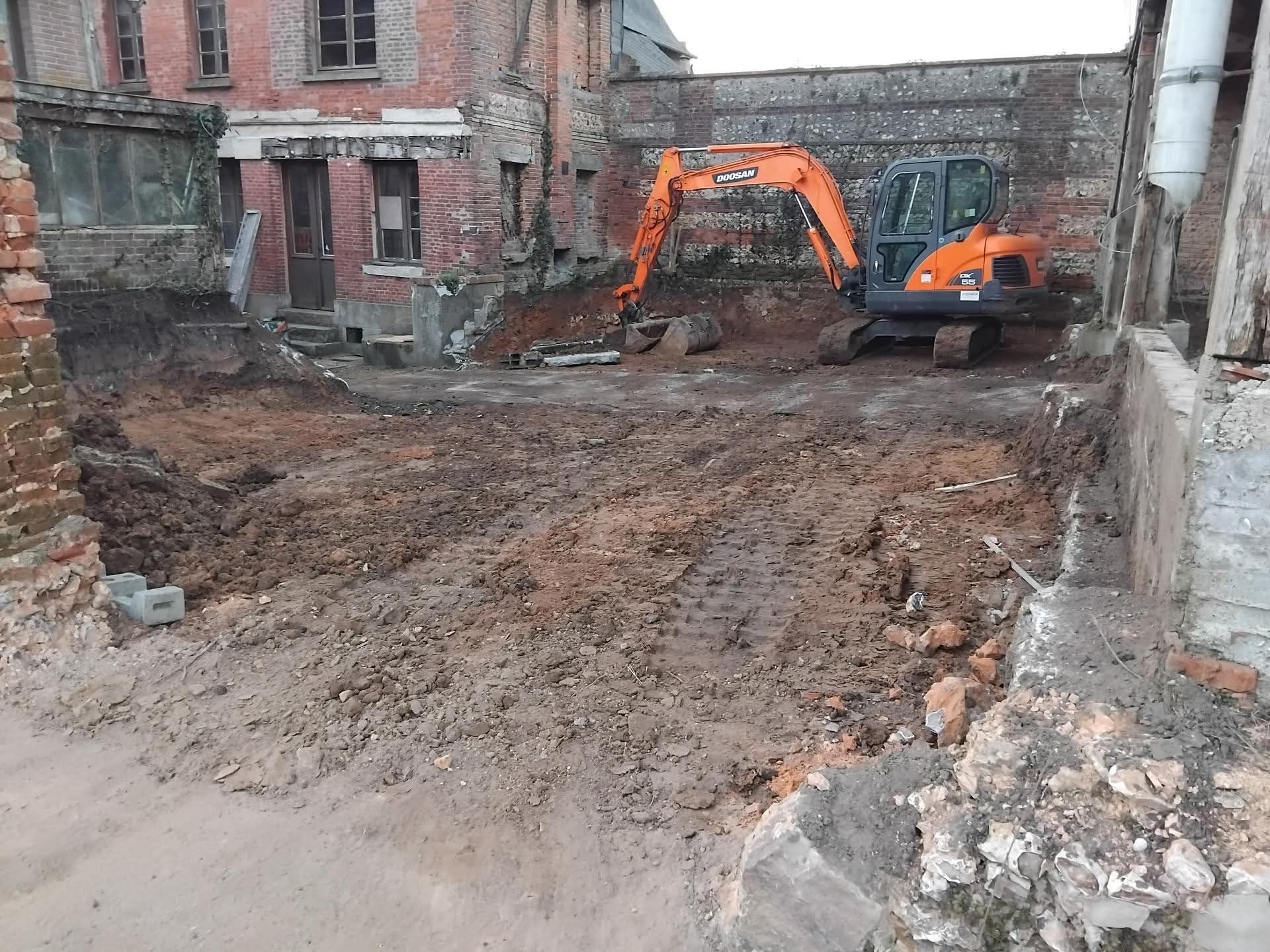 Chantier de construction avec deux pelleteuses orange nivelant un terrain boueux à côté d'un bâtiment en briques.