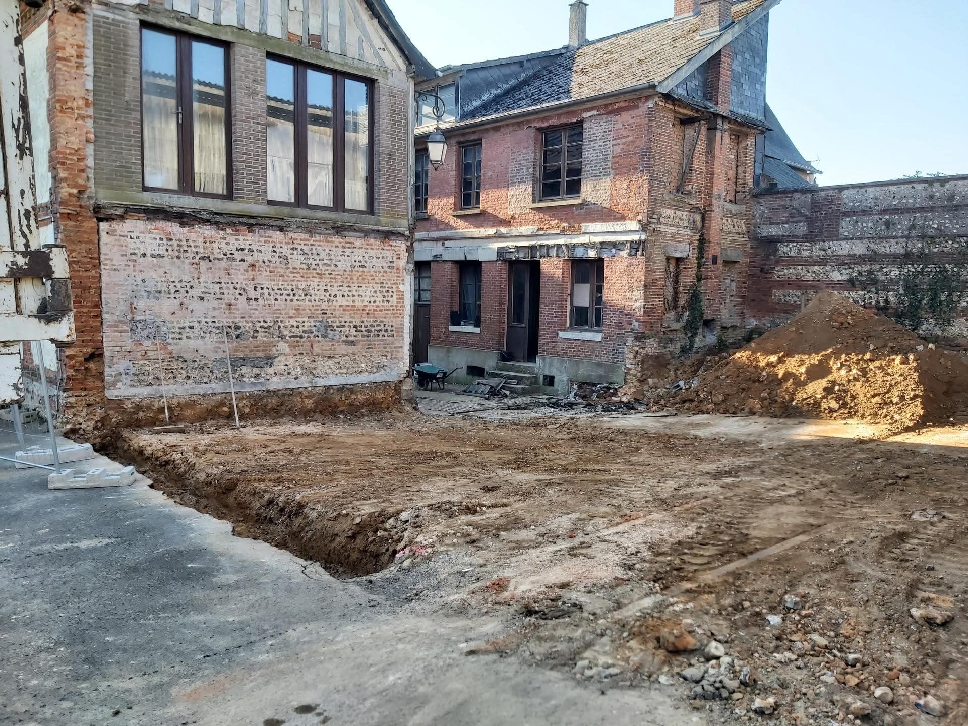 Extérieur de maison en briques inachevé, cour creusée et gravats au sol.