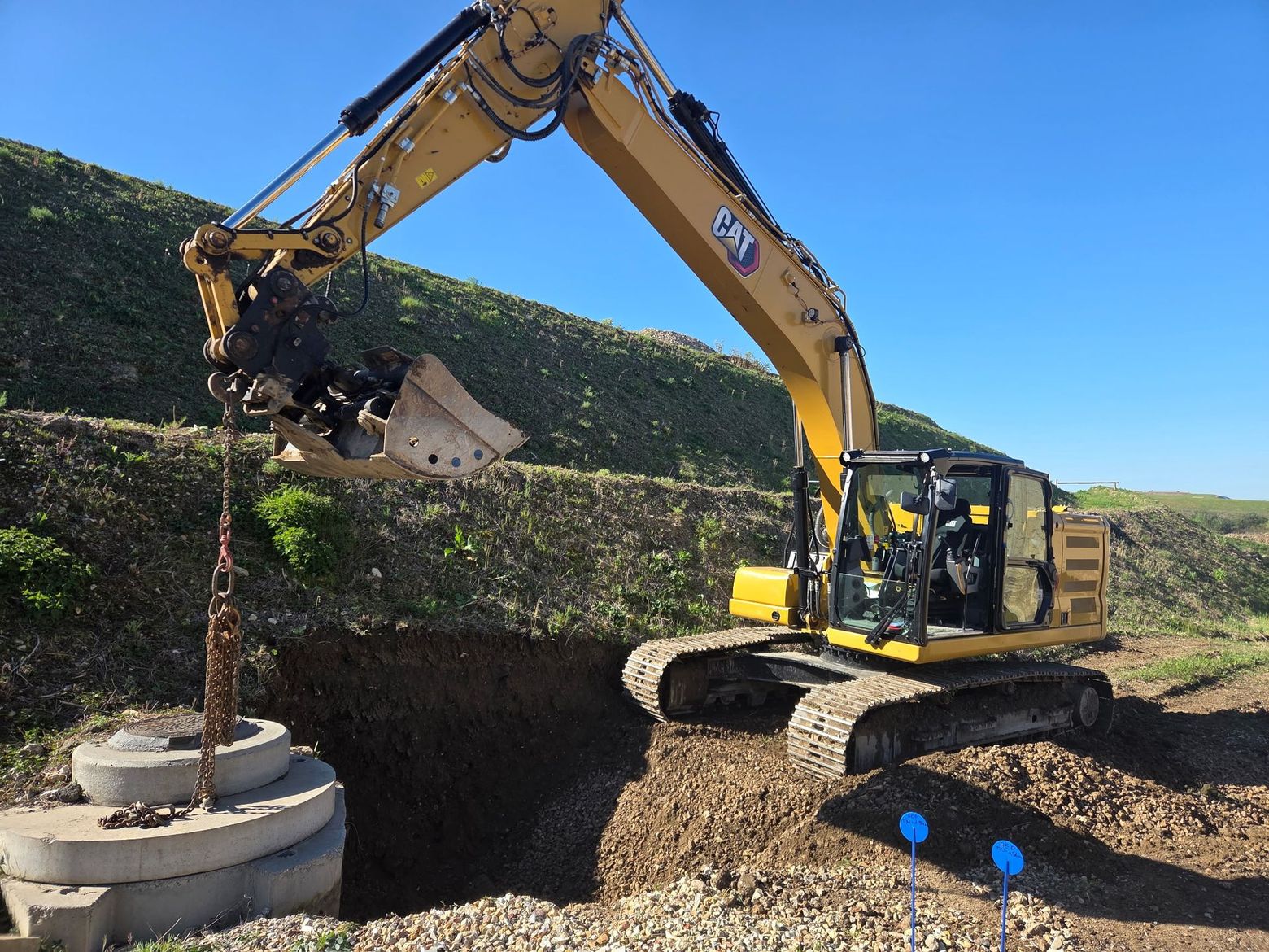 Une excavatrice soulève des débris au bord d'une tranchée sur un chantier de construction sous un ciel bleu.