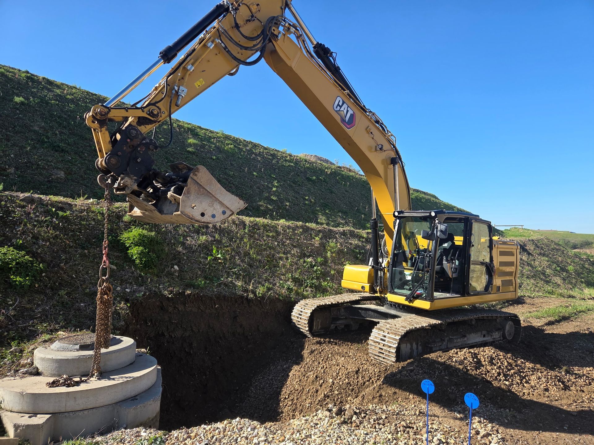 Fosse utilitaire en béton ouverte avec des tuyaux, du gravier et des outils de construction autour.