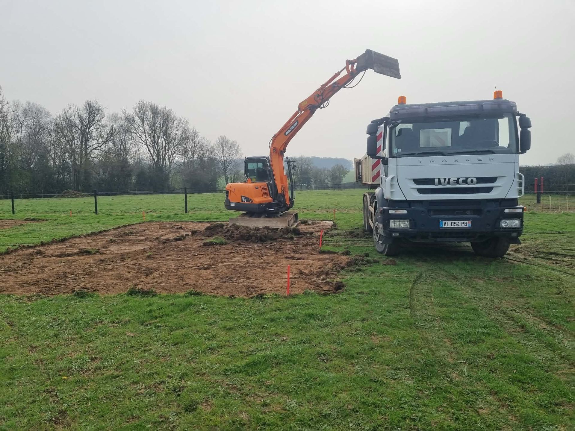 Une excavatrice et un camion blanc sur un chantier boueux dans un champ herbeux.