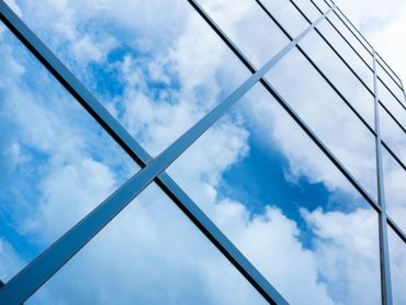 La façade vitrée de l'immeuble reflète le ciel bleu et les nuages.
