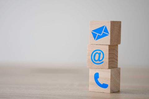 Des blocs de bois empilés avec des icônes bleues de courrier, d'arobase et de téléphone sur une table.