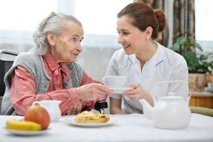 Pflegerin hilft alter Dame bei Kaffee und Kuchen