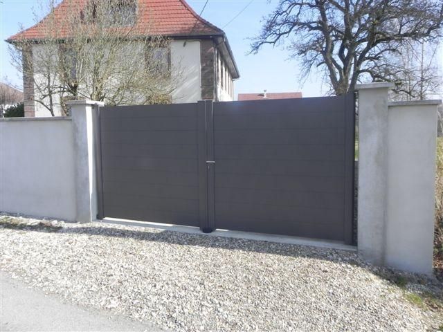 Un portail gris avec des murets en pierre.