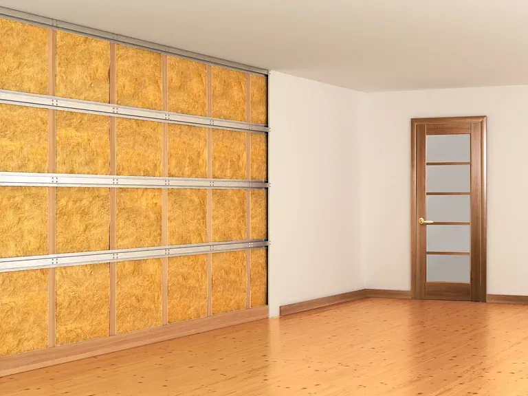Interior de una habitación con aislamiento acústico instalado en una pared. También se ven una puerta y un suelo de madera.