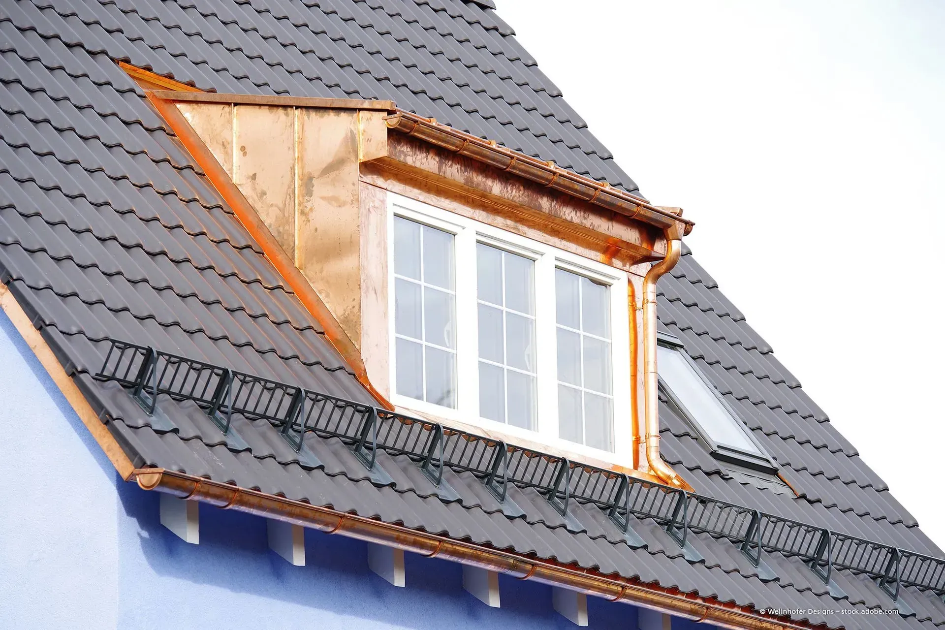 Dachgaubenfenster im Bau auf einem steilen grauen Dach, darunter freiliegendes Holzfachwerk und blaue Wand