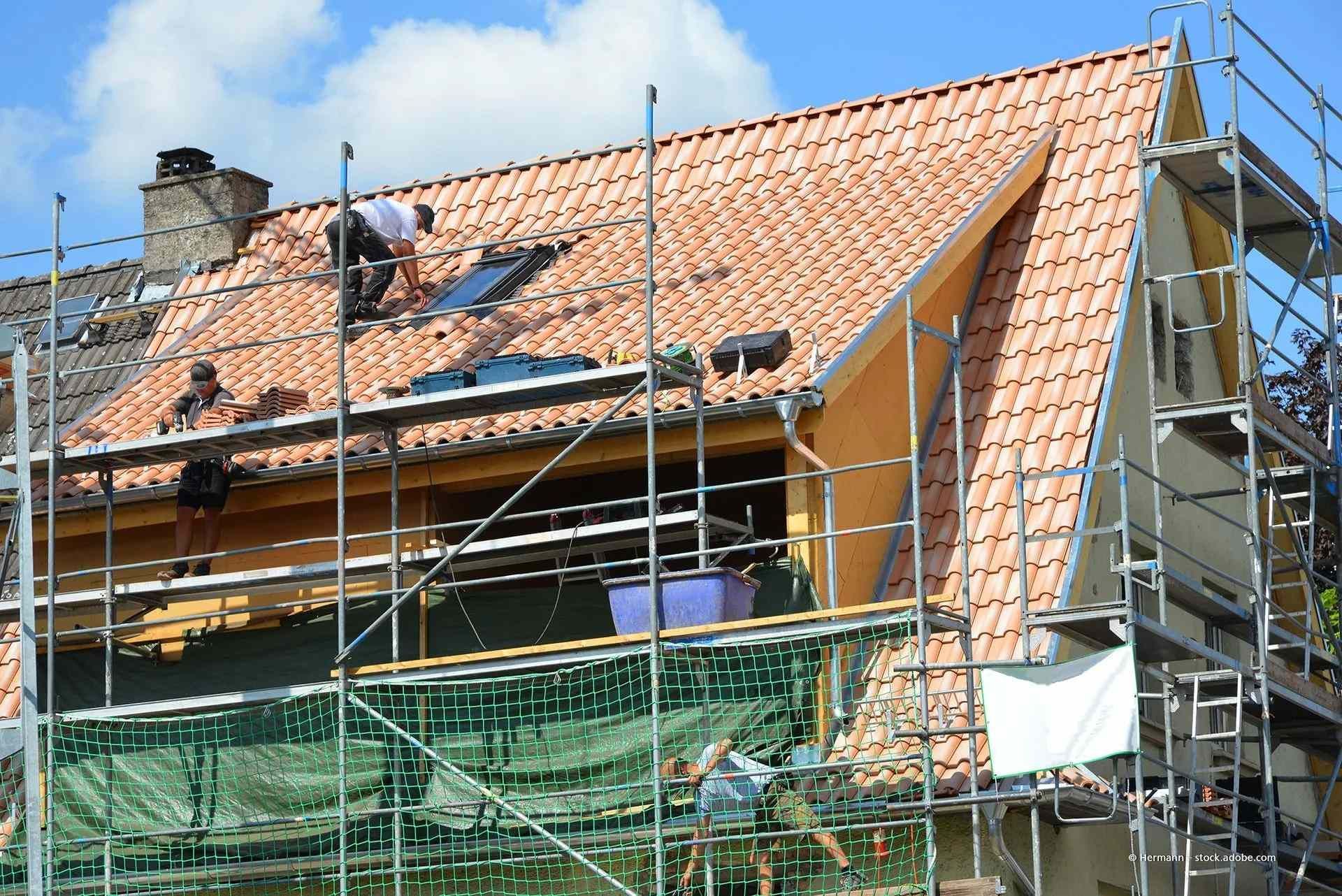 Hausdach wird unter blauem Himmel mit Gerüst und grünem Netz repariert