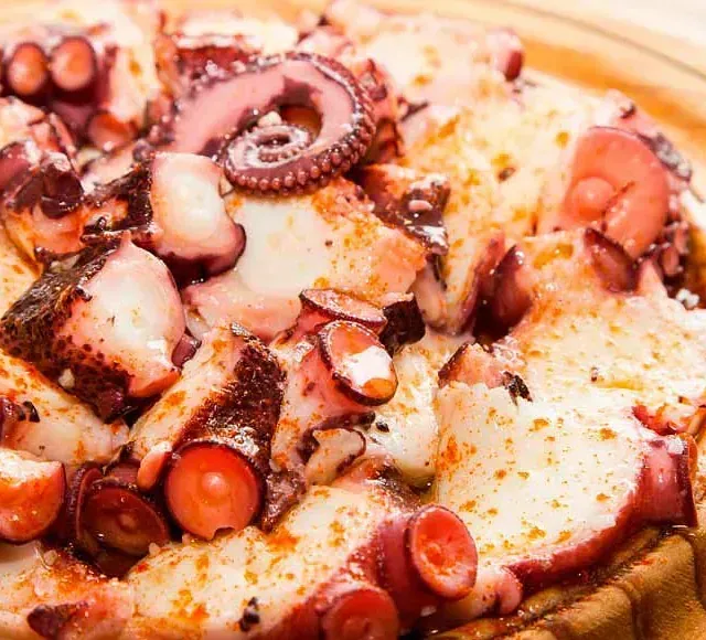 Una pizza con pulpo encima, sobre un plato de madera.
