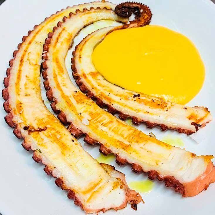 Un plato blanco cubierto con rodajas de pulpo y salsa amarilla.