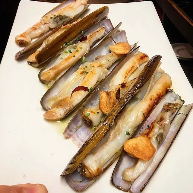 Un plato blanco cubierto con una variedad de mariscos, incluidas vieiras.