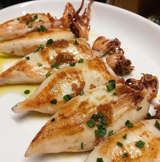 Un plato blanco cubierto con calamares y cebollas verdes.