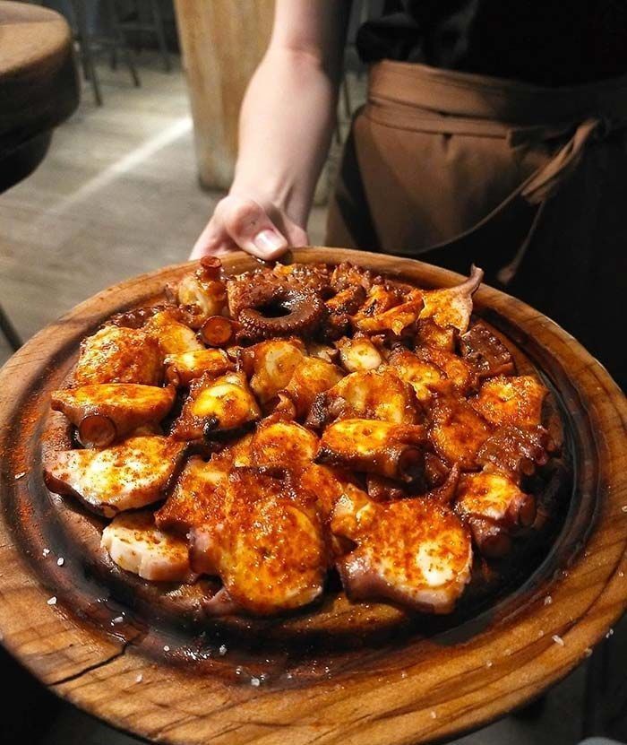 Una persona sostiene un plato de madera con comida.