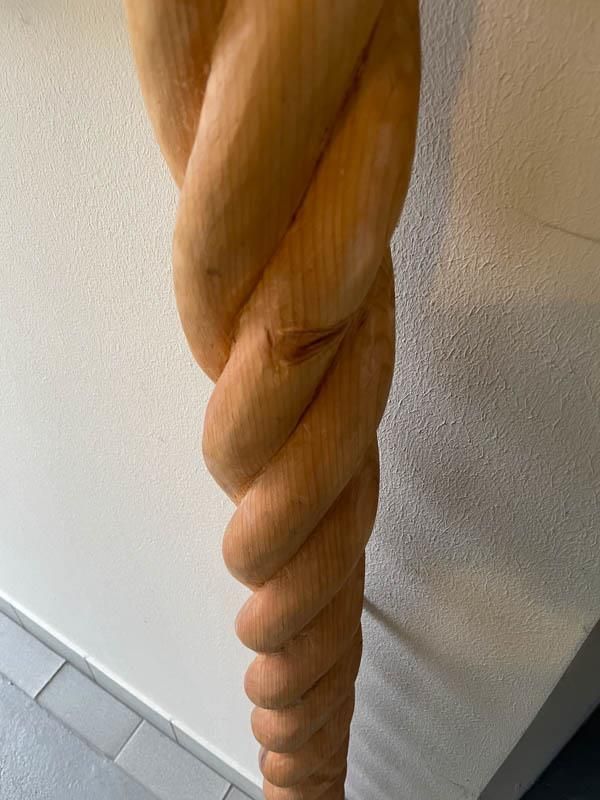 Eine Holzskulptur eines gedrehten Seils vor einer weißen Wand.