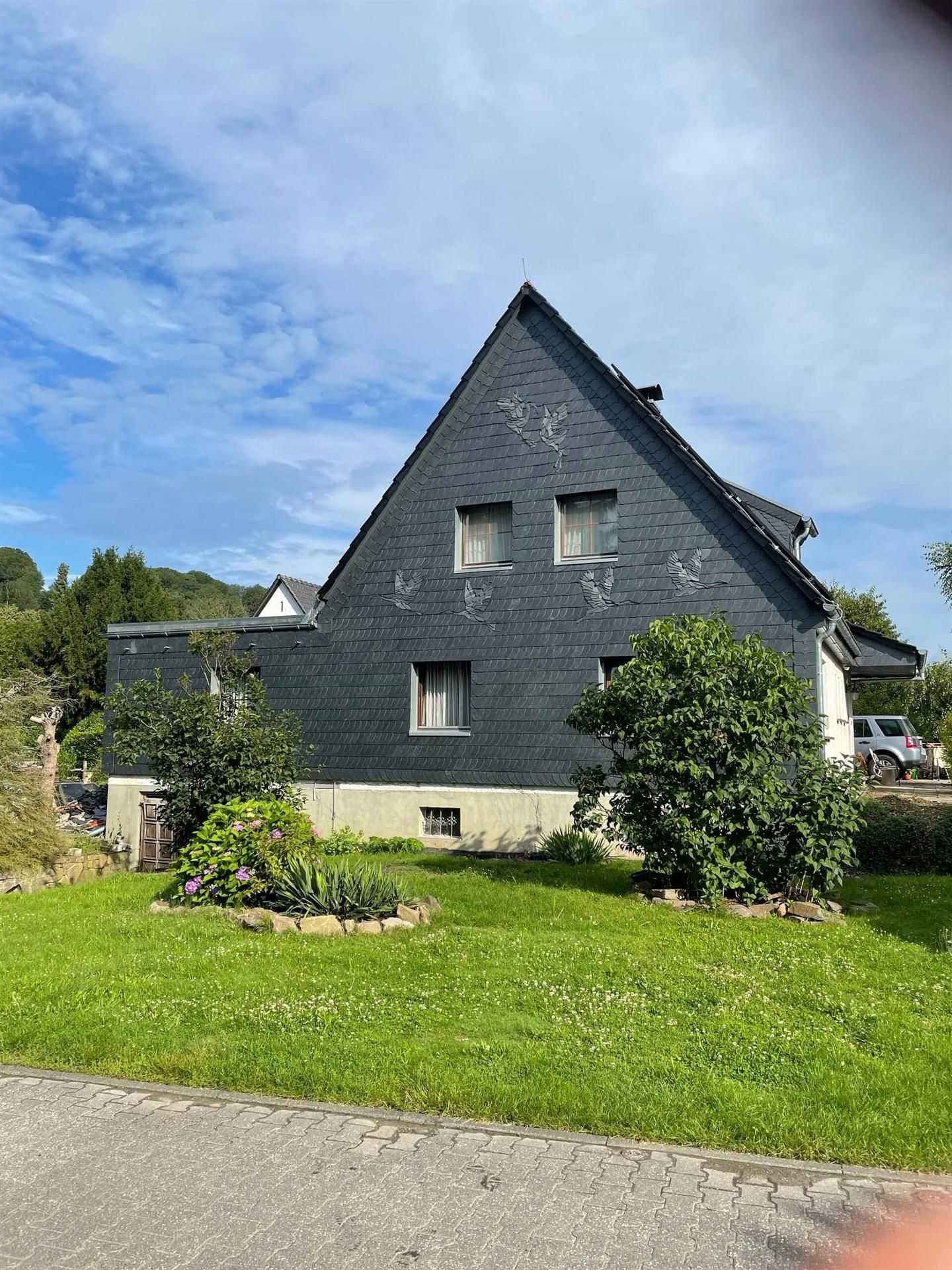 Ein Haus mit Schieferdach ist von einem üppig grünen Garten umgeben.