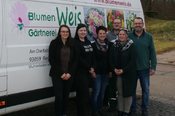 Eine Gruppe von sechs Personen steht lächelnd vor einem weißen Lieferwagen mit dem Logo „Blumen Weis Gärtnerei“.