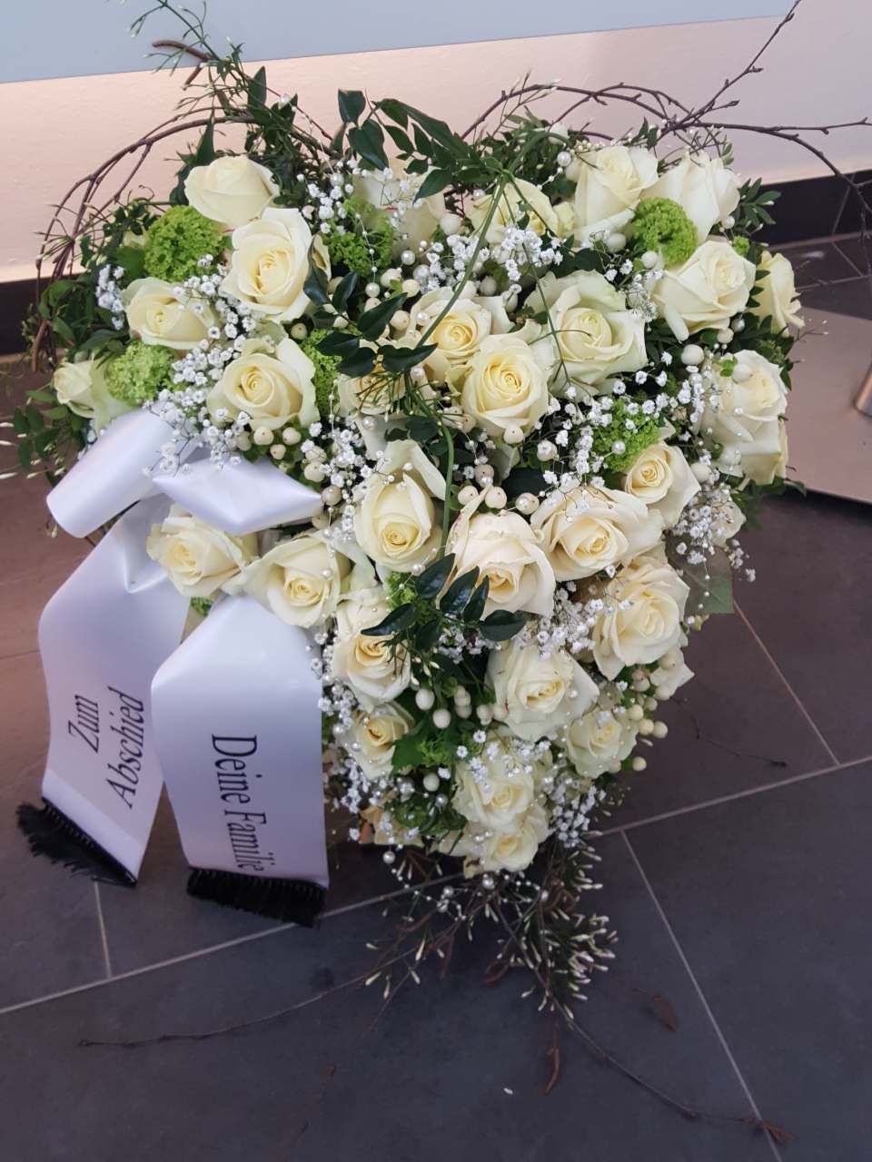 Gesteck aus weißen Rosen mit Schleife; eine Hommage.
