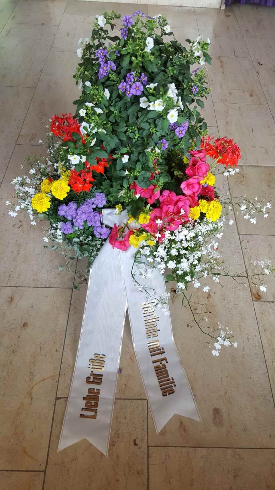 Blumenkranz mit bunten Blumen und weißem Band; goldener Schriftzug „Liebe für uns“ und „Familie“.