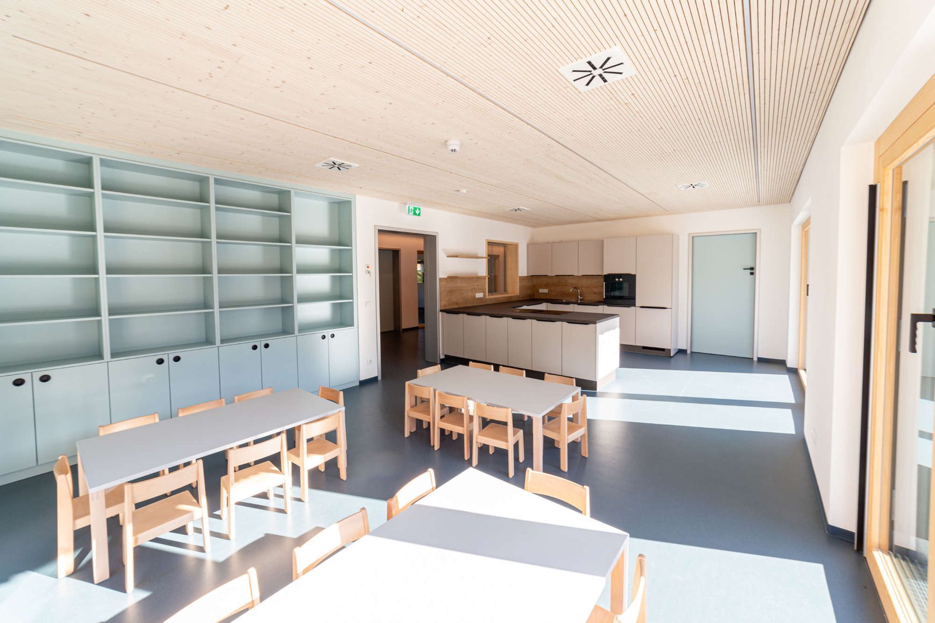 Zimmereinrichtung in hellen Pastelltönen mit hohen Schränken, einer Küchenzeile und Esstischen