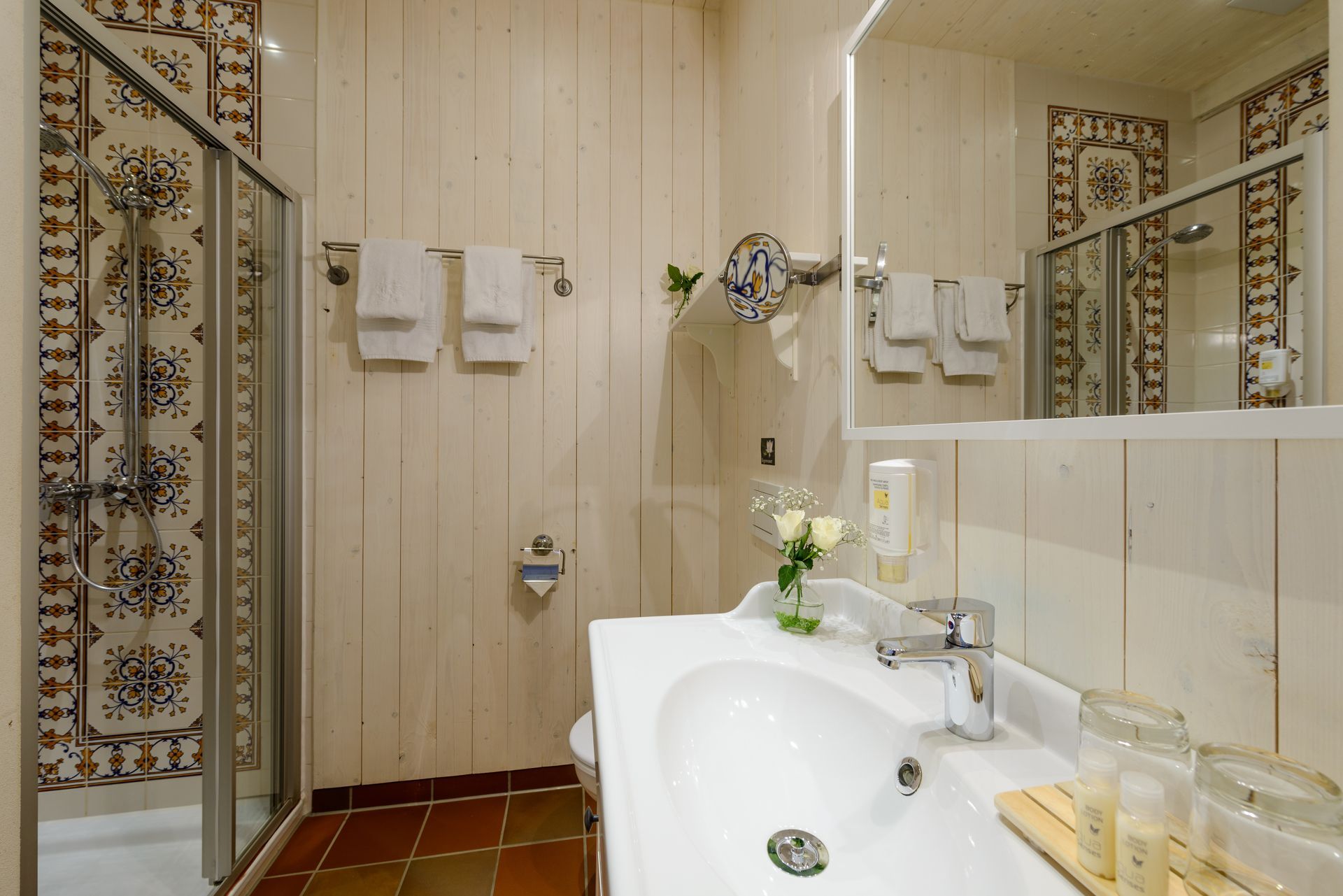 Badezimmer mit weißem Waschbecken, Dusche und gemusterten Fliesenakzenten.