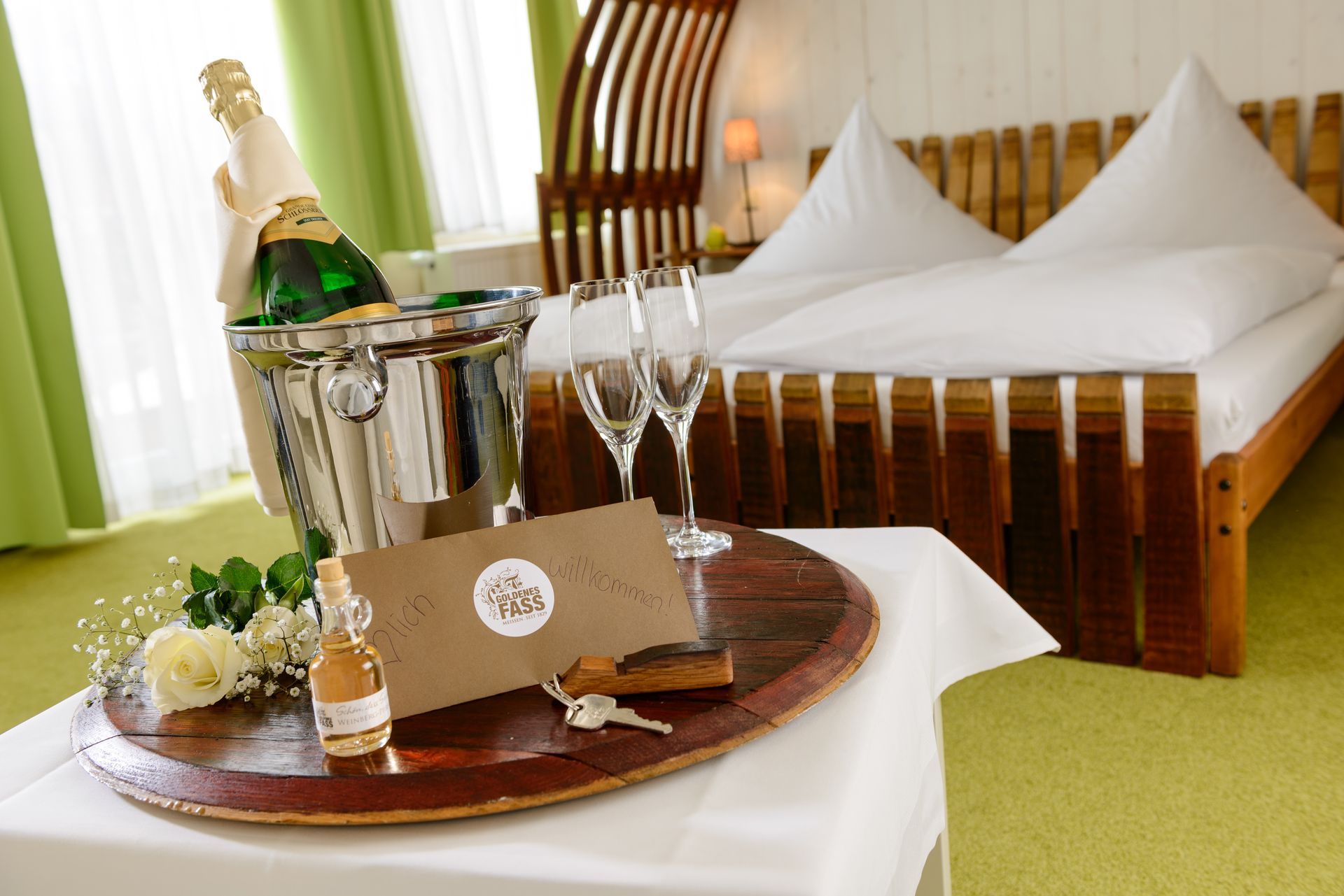 Hotelzimmer mit Champagner, Gläsern und einer Willkommensnachricht auf einem Tablett neben dem Bett.